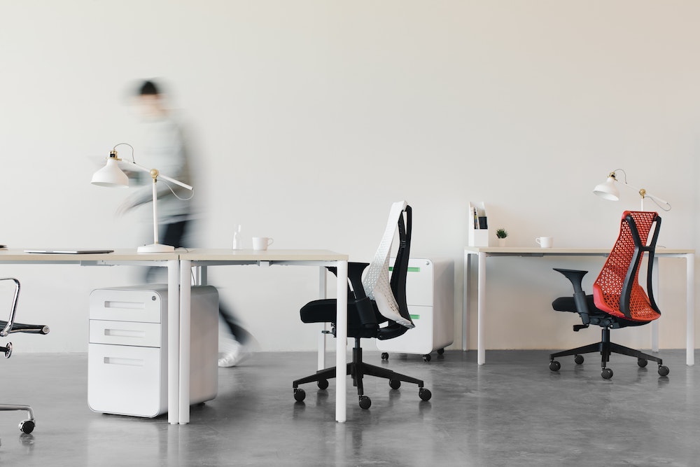 Spacious office showing desks and chairs, with someone walking by