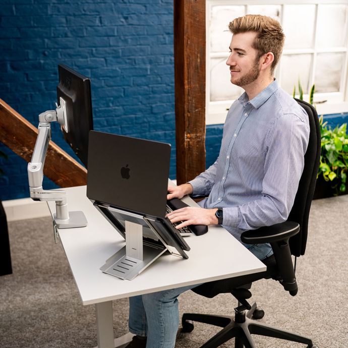 KOJI White Electric Sit-Stand Desk - lifestyle shot, shown lowered in seated position