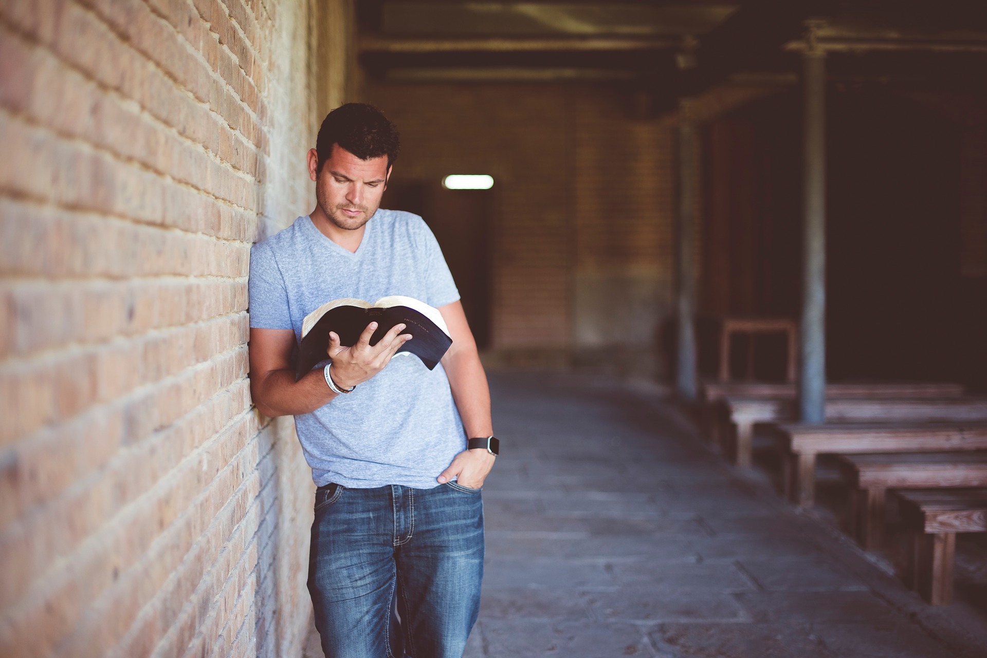 Man reading a book while leaning against a brick wall