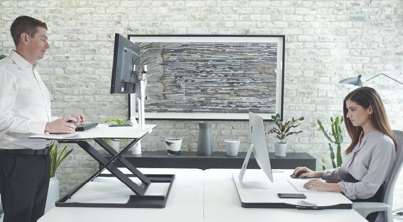 Two people using a Oploft Sit-Stand Platform opposite each other, one using it standing up, the other in a seat position