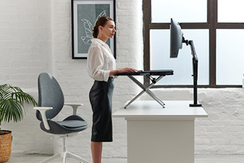 Monto Sit-Stand Riser shown raised with a woman working standing up