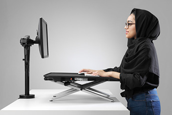Woman standing at her desk, using the Monto Sit-Stand Riser in the raised position
