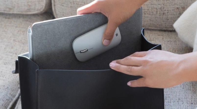 Image of someone packing their office accessories: including their tablet and Microsoft Modern Mobile Bluetooth Mouse in their bag - showcasing how great the mouse is for on-the-go workers / hybrid workers