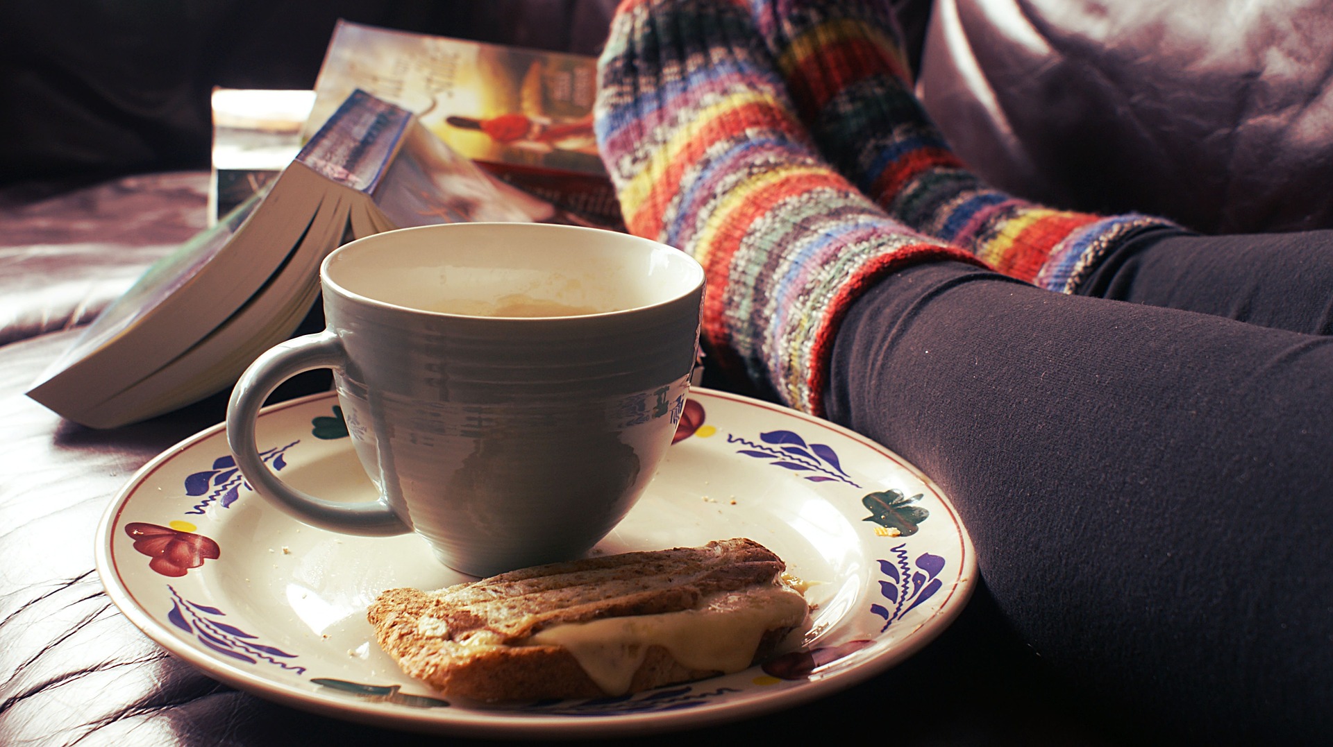 Close up of a tea cup with a cake on the saucer, and a woman's feet up relaxing